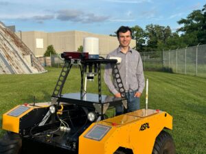Alexander Krawciw standing on the field behind an offroad robotics vehicle